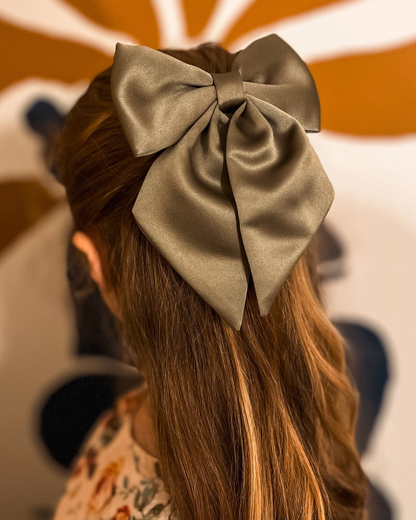 Person with long hair wearing a large green bow, with a colorful abstract background.