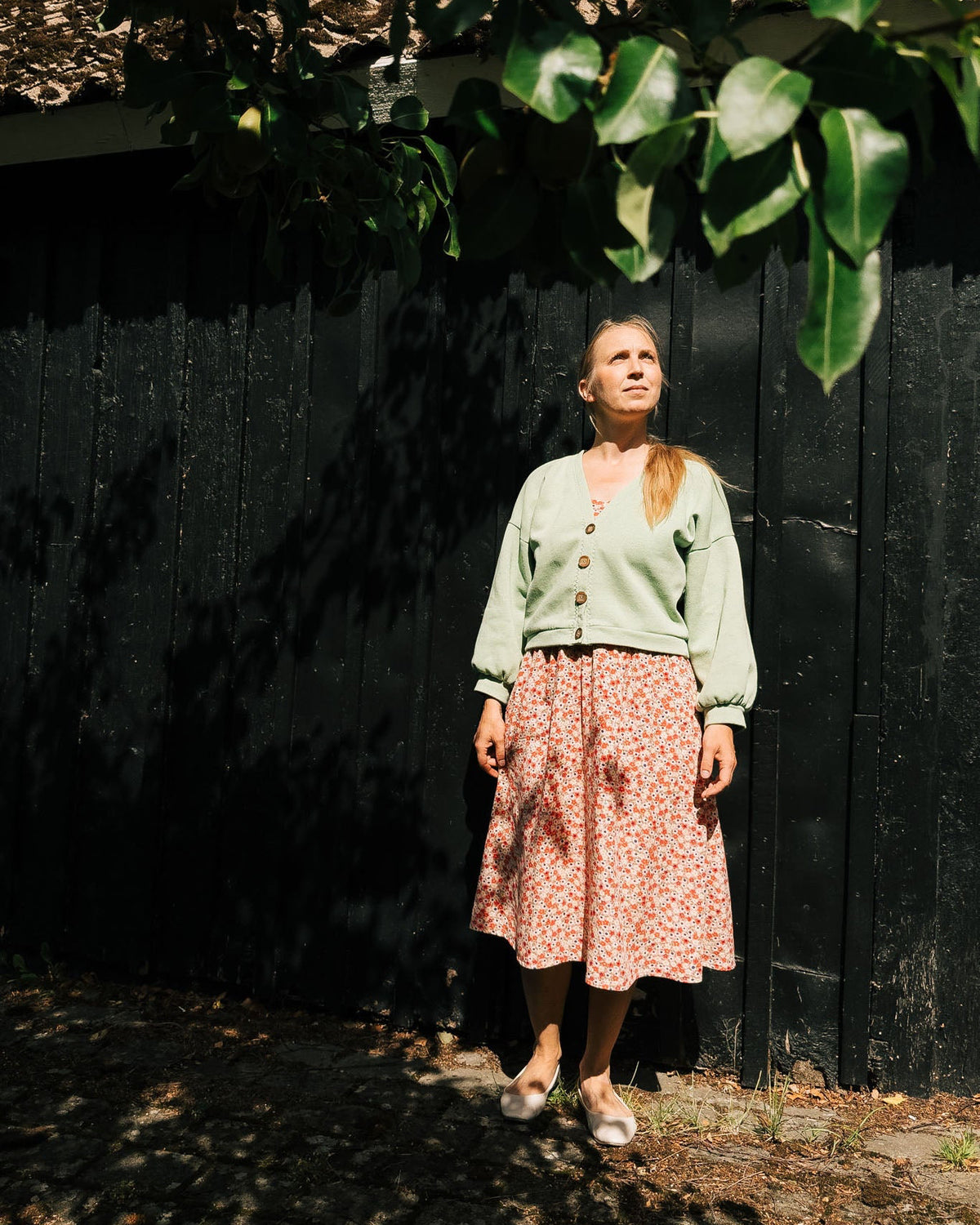 Woman standing against a dark wall with greenery above