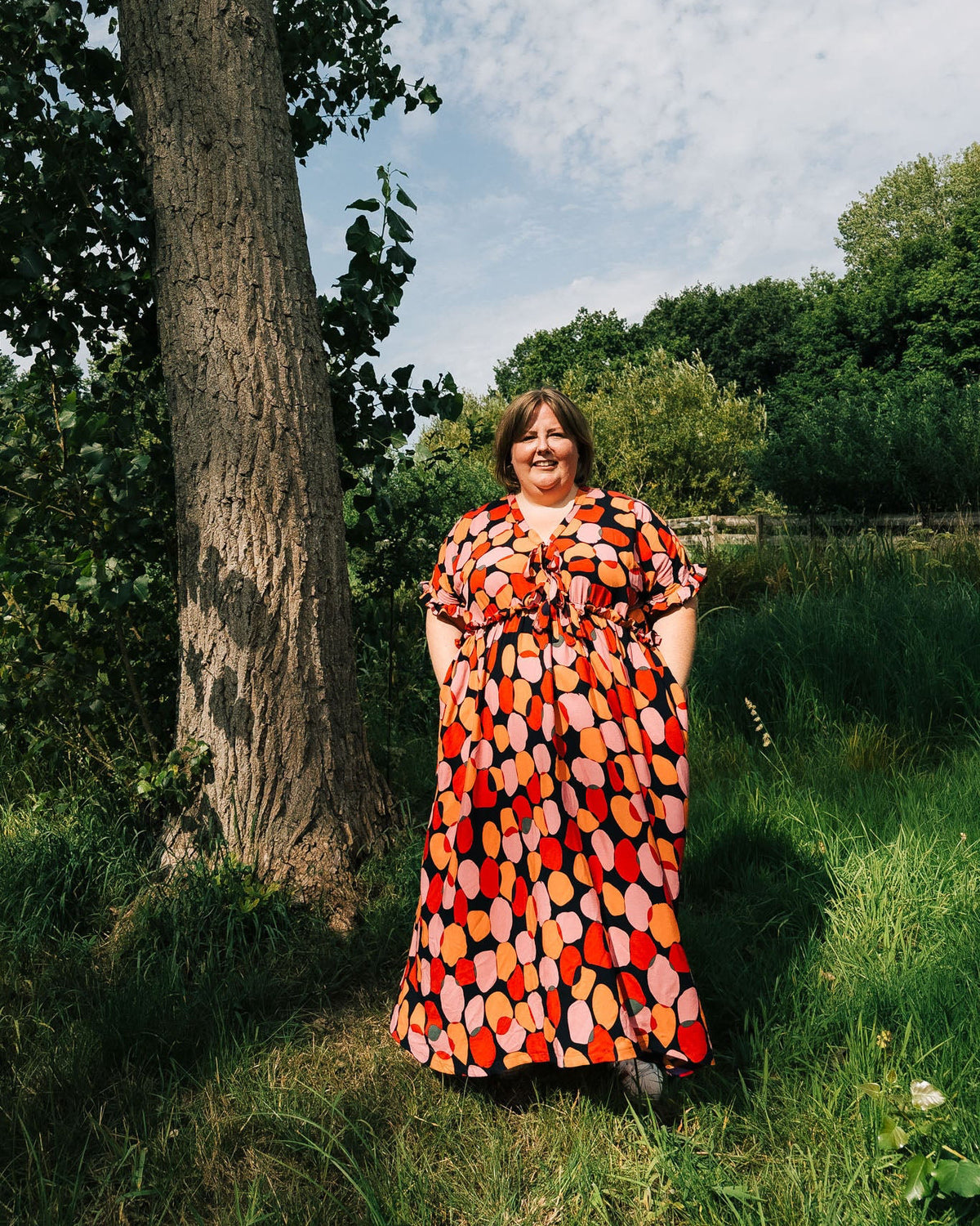 Woman in a colorful dress standing by a tree in a park