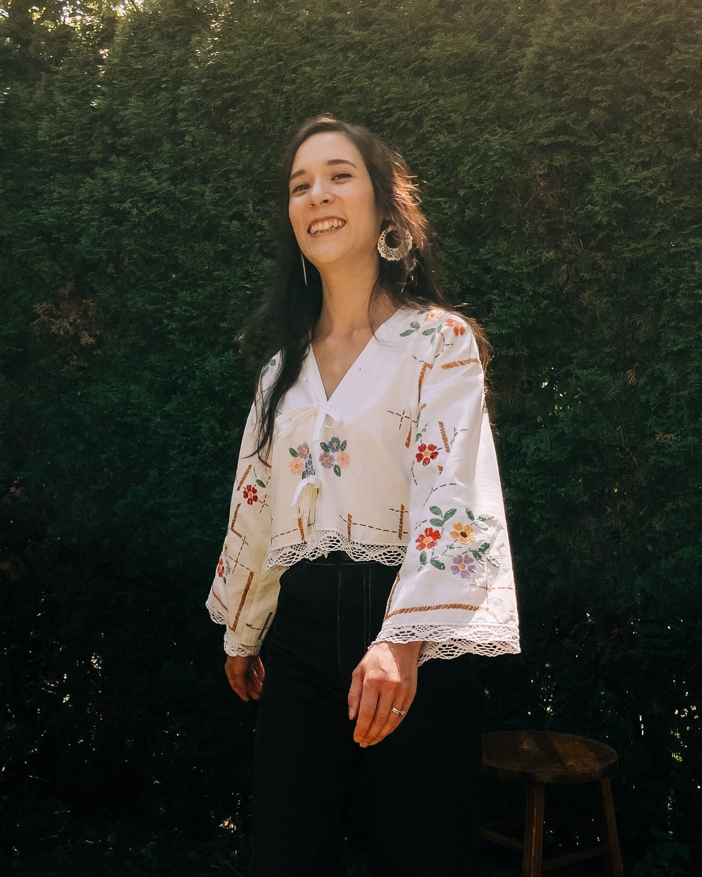 Woman wearing a floral blouse standing outdoors with greenery in the background