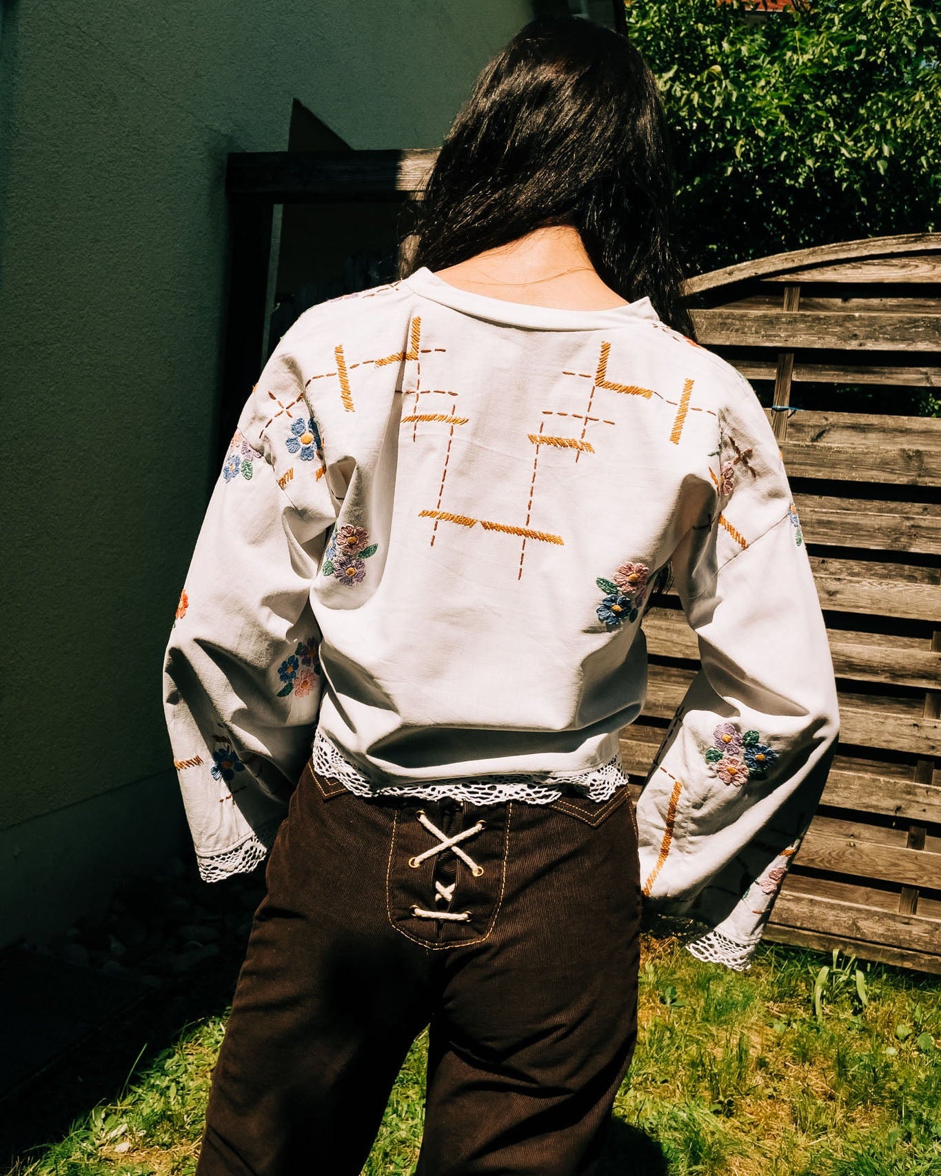 Person wearing a white embroidered jacket and brown pants standing outdoors.
