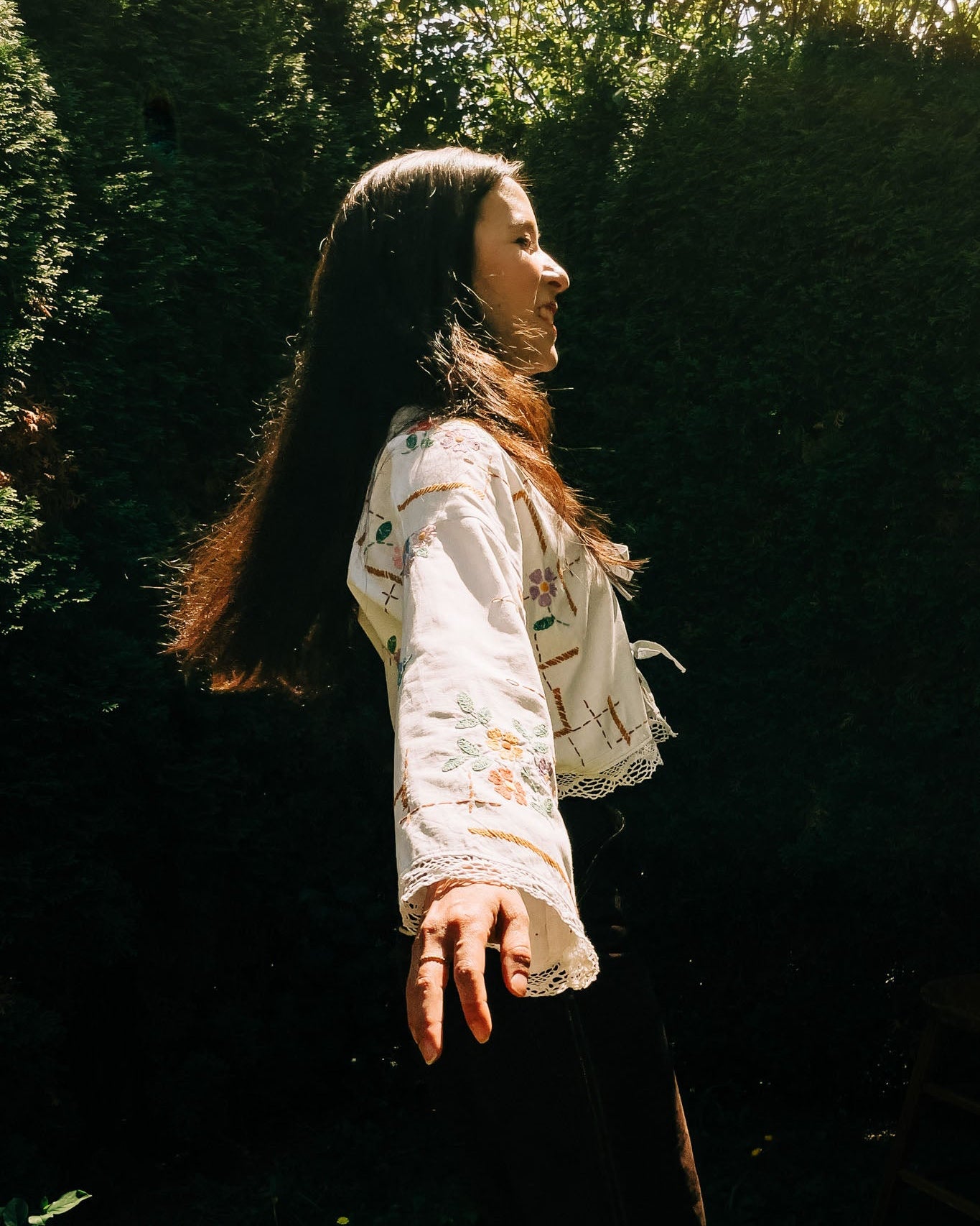 Woman in a floral blouse standing among trees with a warm, natural light.