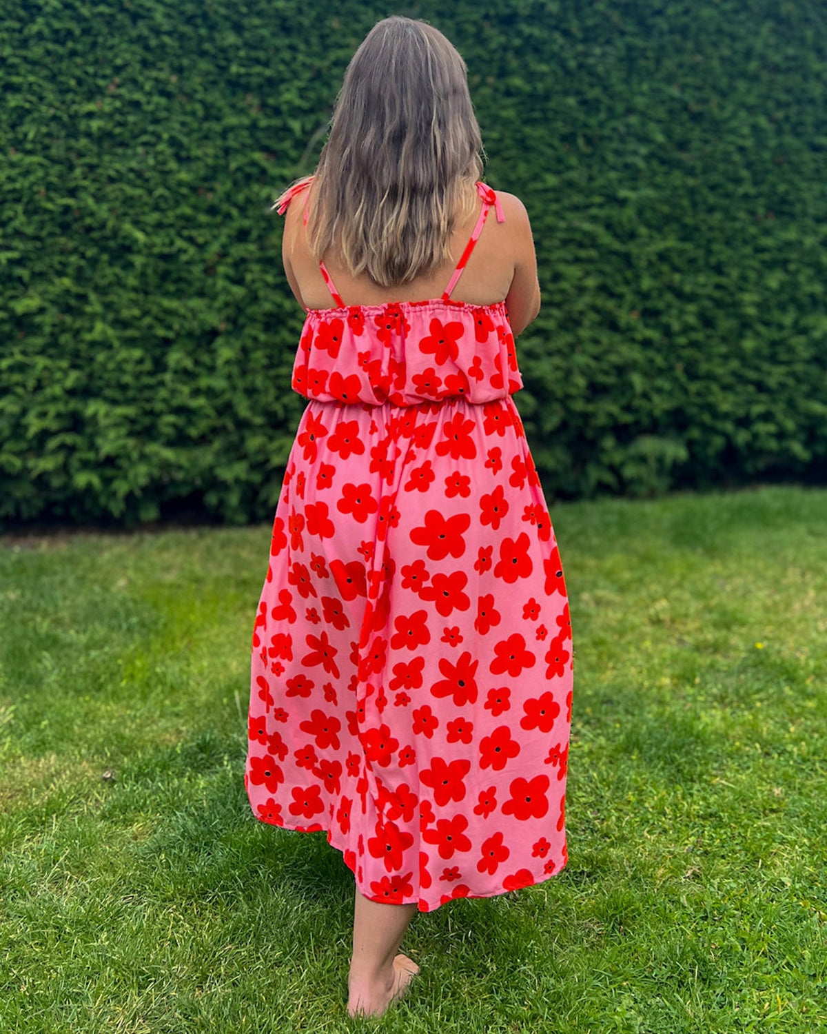 Woman in a red floral dress standing on grass with a hedge in the background