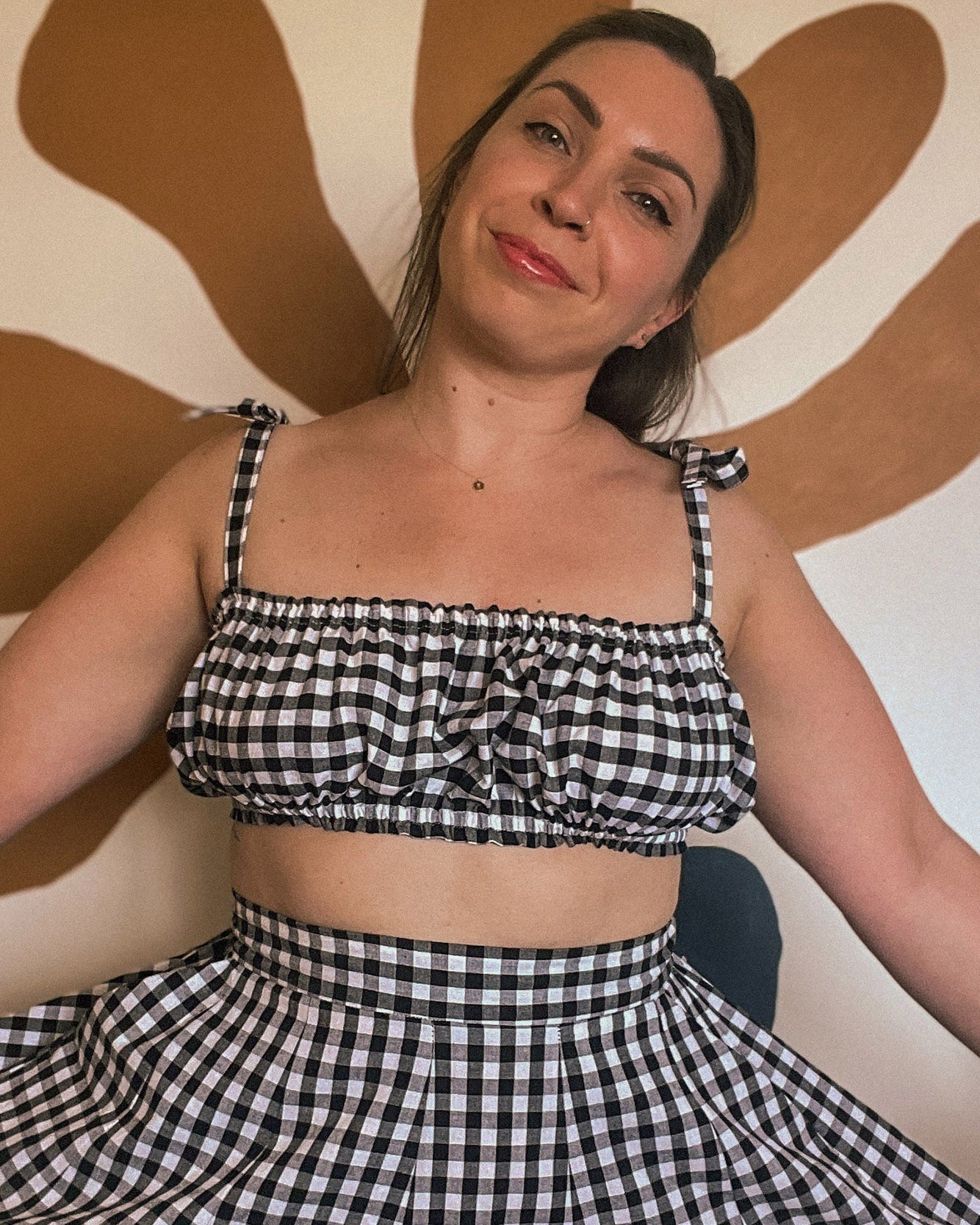 Woman wearing a black and white checkered outfit against a brown abstract wall.