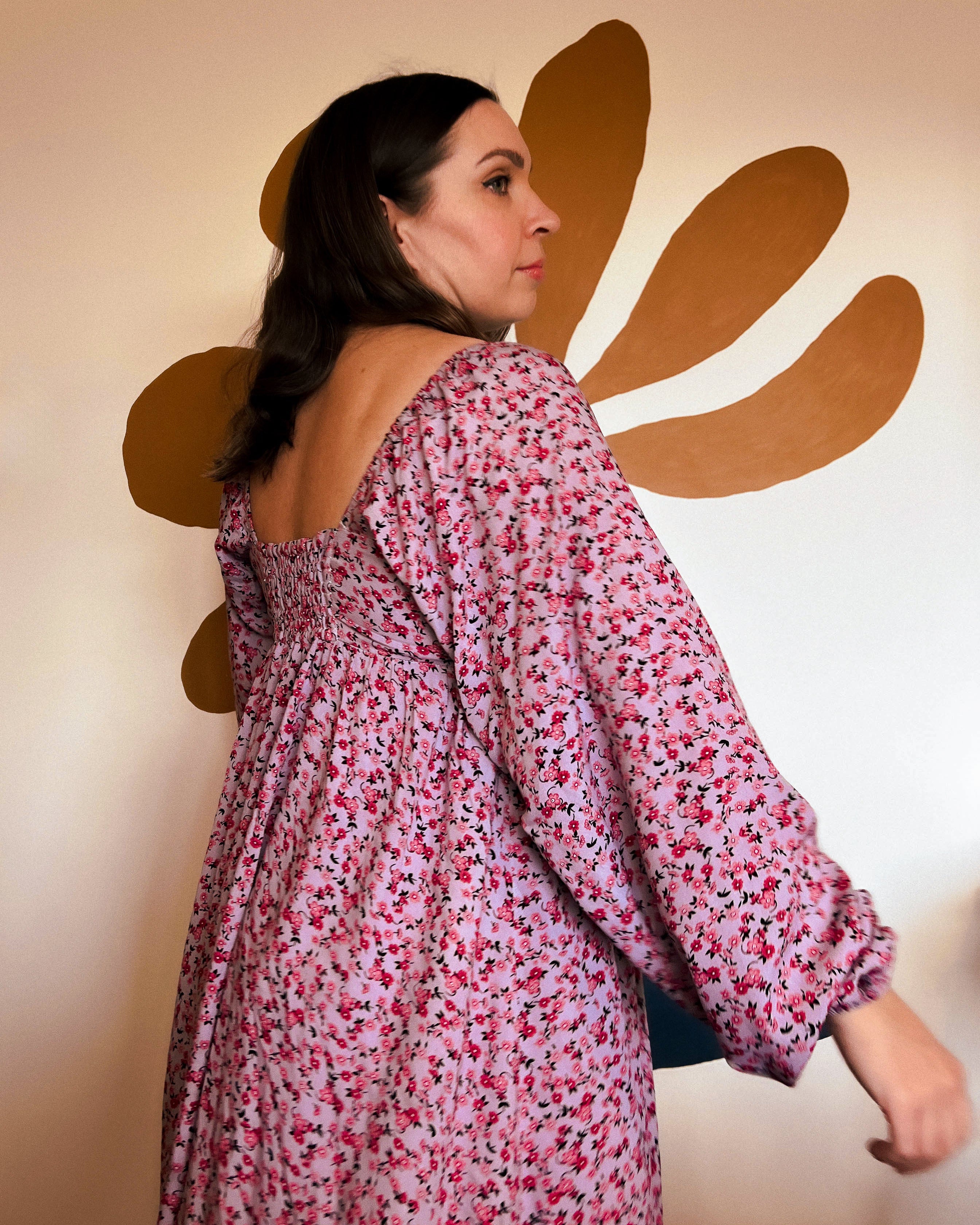 Woman wearing a floral dress with a decorative wall in the background