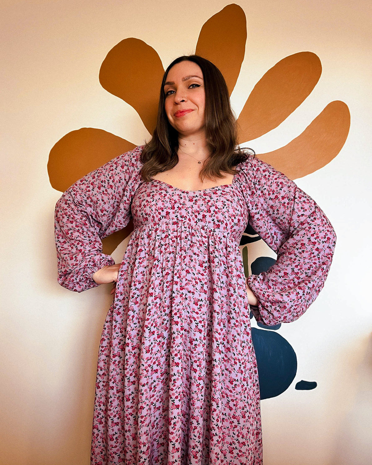 Woman in a floral dress standing in front of a decorative wall with a large flower.