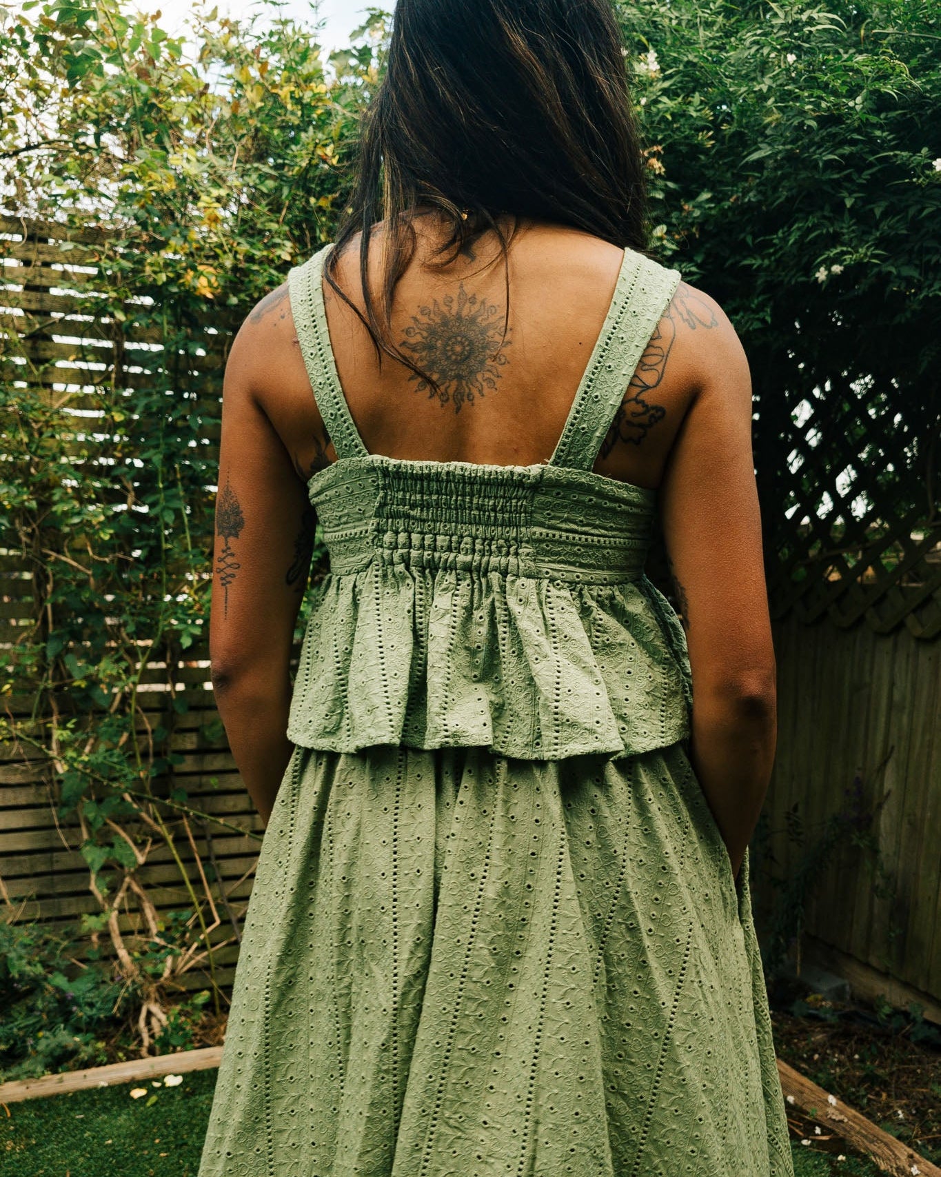 Person wearing a green dress with a textured pattern, standing outdoors with greenery in the background.