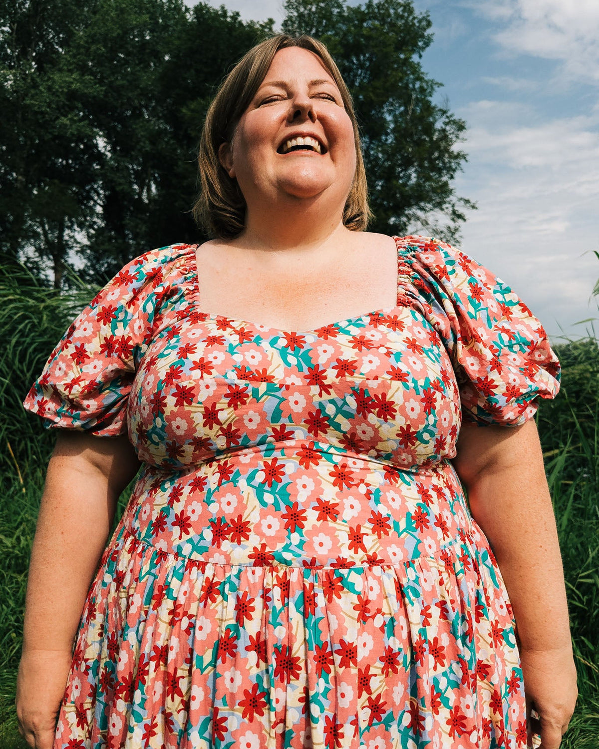 Woman wearing a floral dress standing outdoors with trees and blue sky in the background