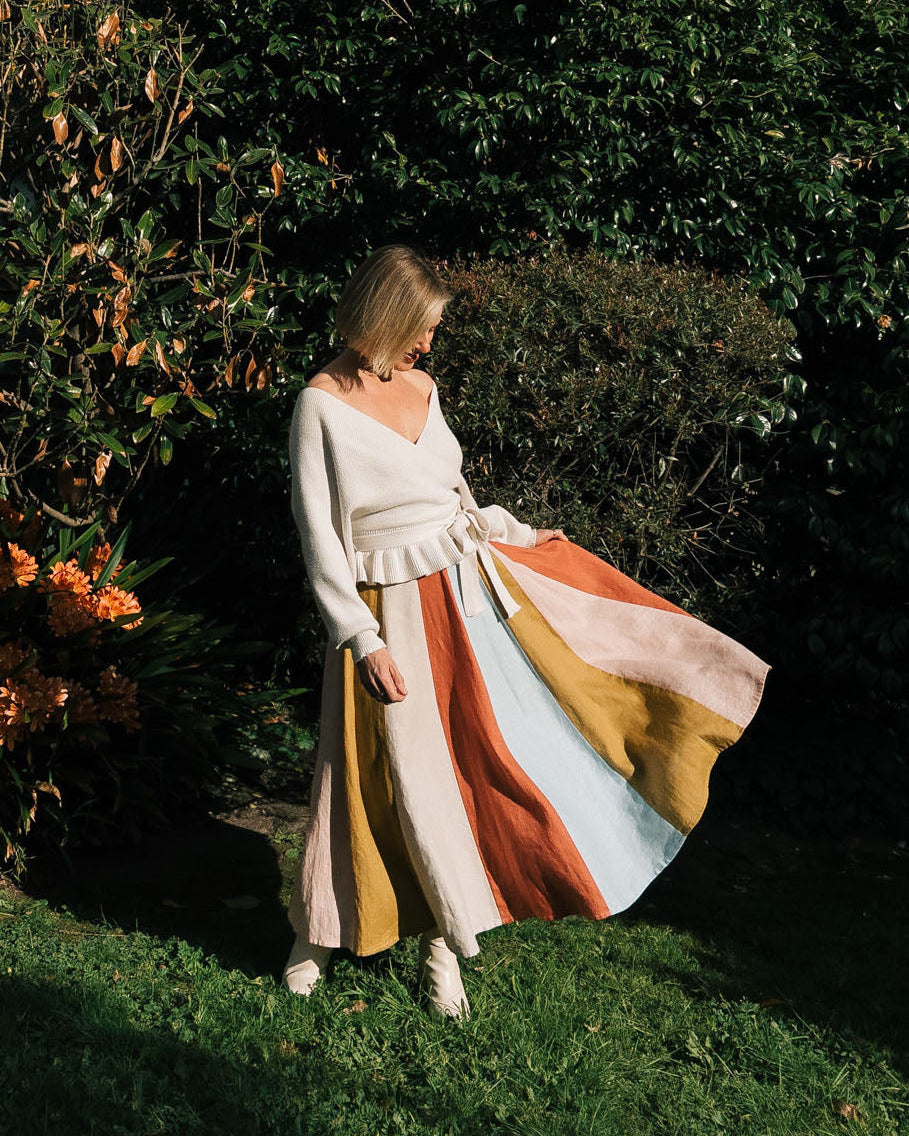 Woman in a white top and colorful skirt standing in a garden.