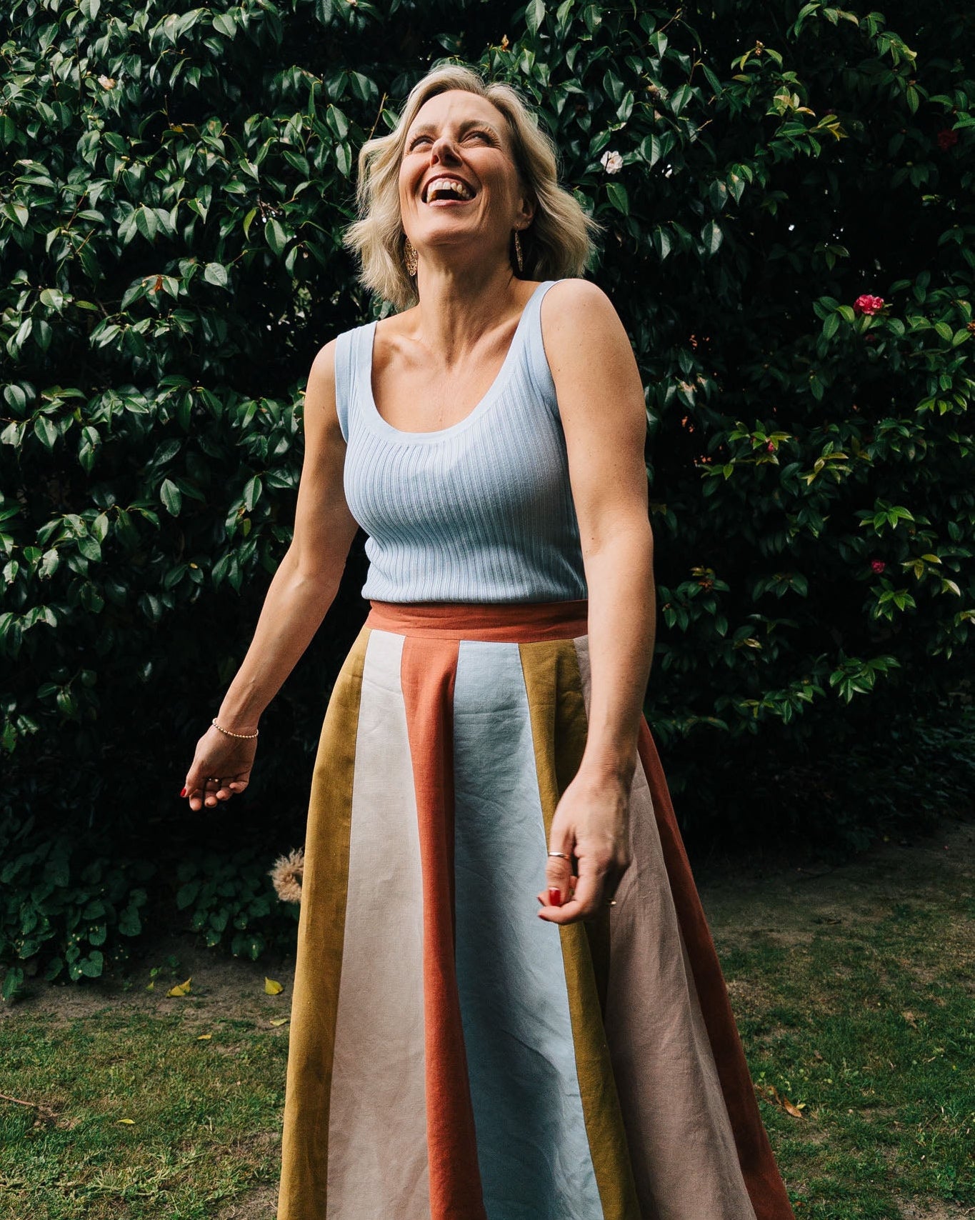 Woman laughing outdoors with a green bush and flowers in the background