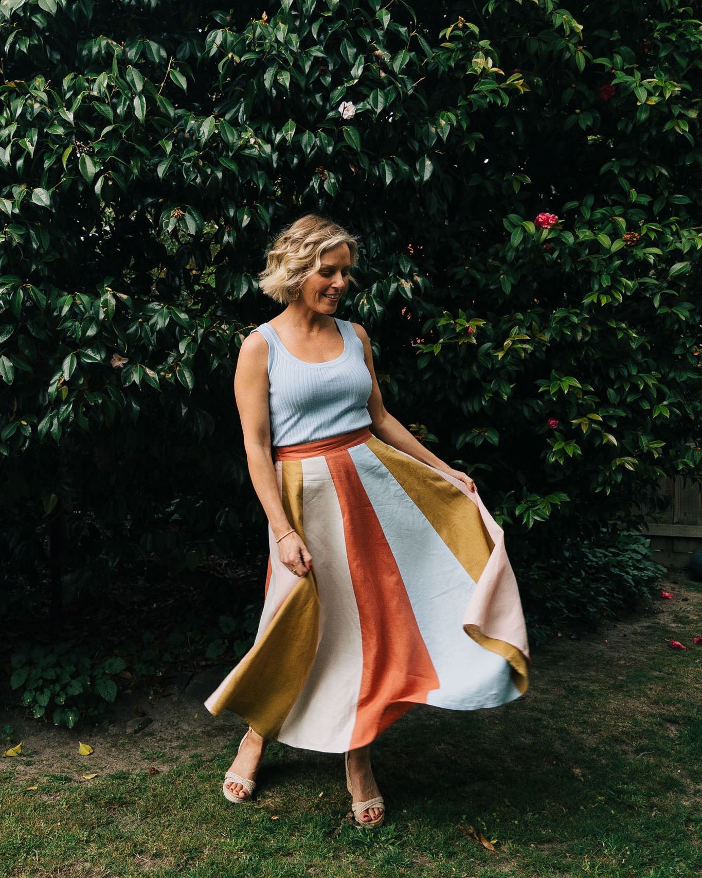Woman in a colorful skirt standing in front of a leafy green wall.