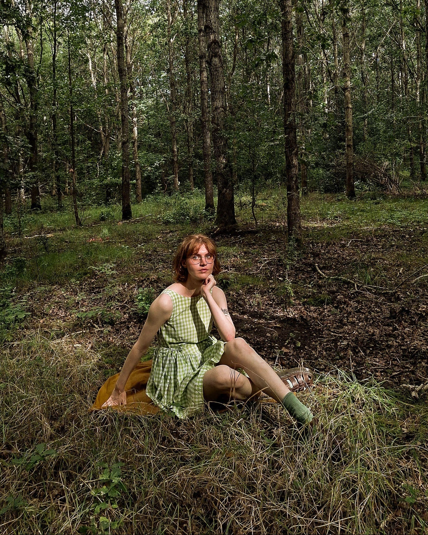 Person sitting in a forest wearing a green dress.