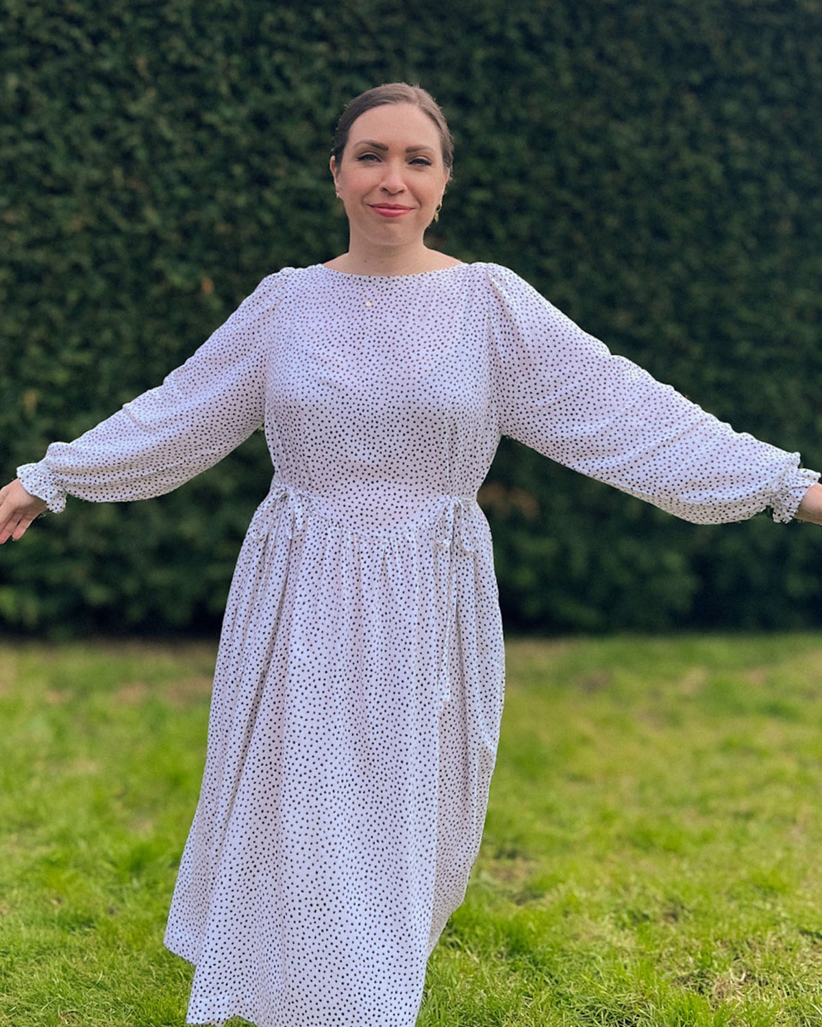 Woman in a white dress standing in a grassy area with green bushes in the background