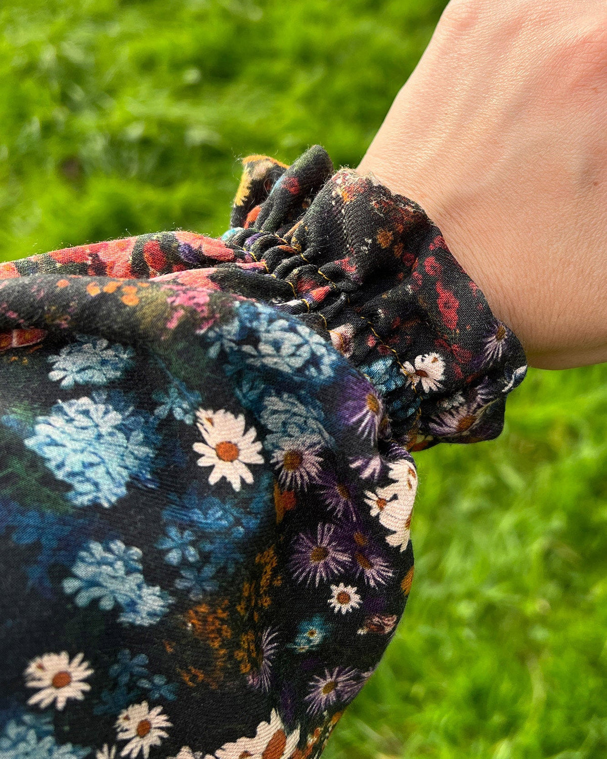 Floral-patterned scrunchie on a wrist with grass in the background