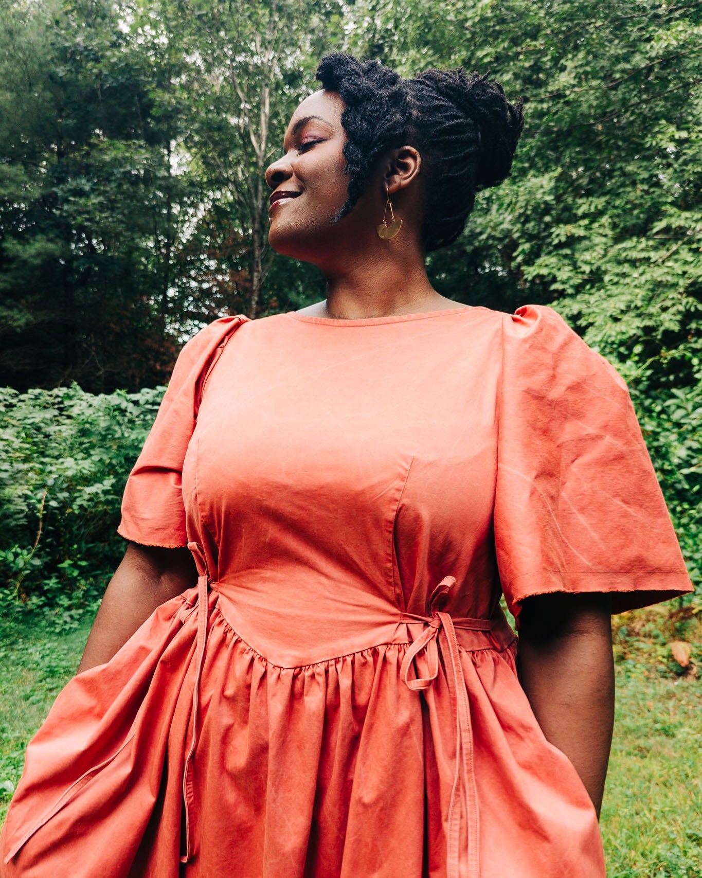 Woman wearing a coral dress standing outdoors with greenery in the background