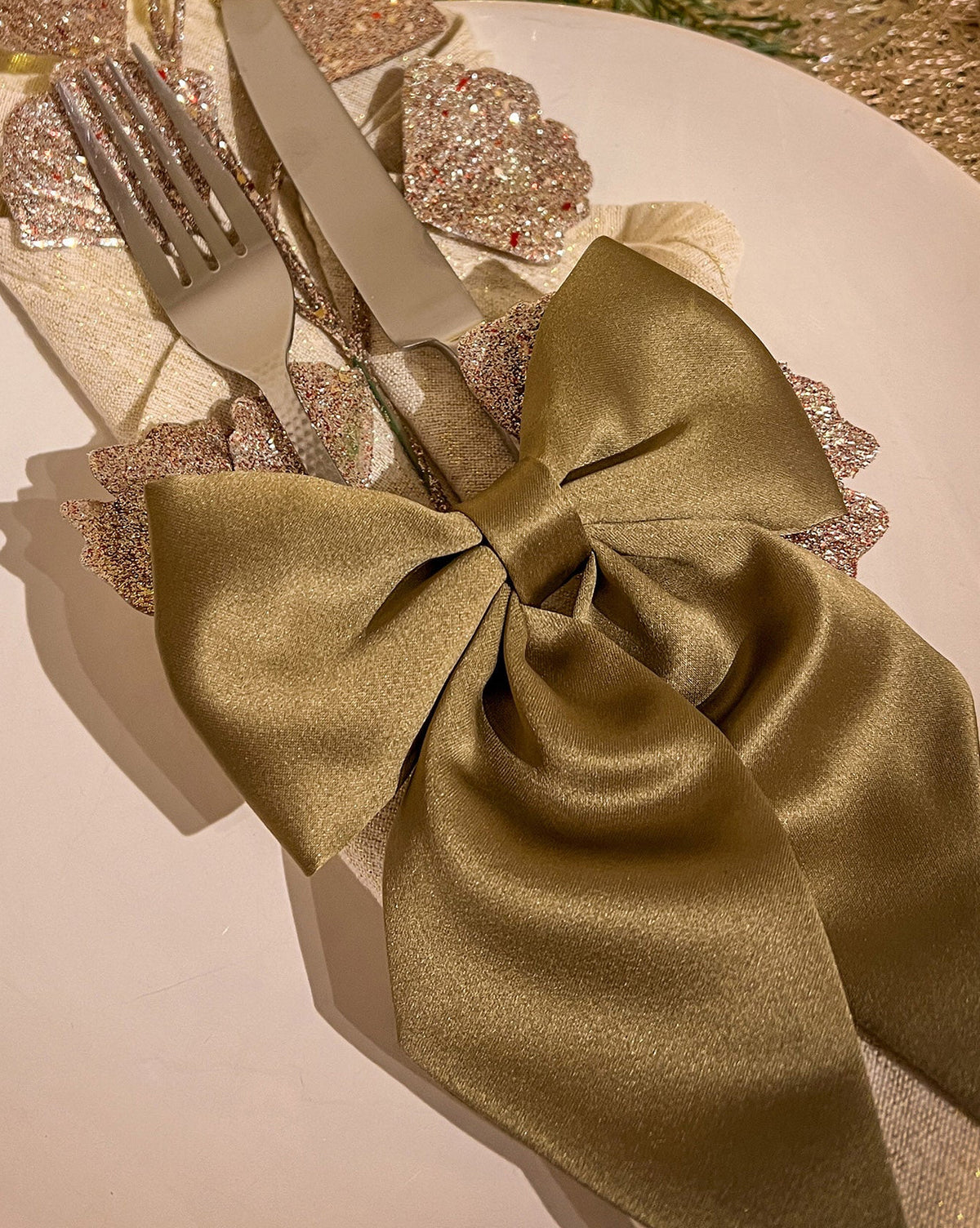 Gold napkin tied in a bow with cutlery on a festive table setting.