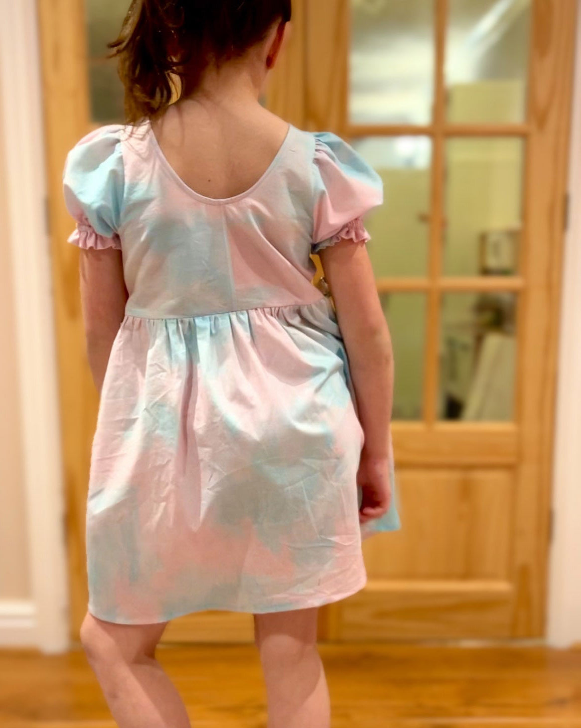 Child wearing a pastel dress with puffed sleeves in a home setting.
