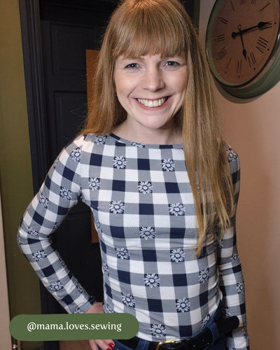 Woman wearing a blue and white checkered shirt with floral patterns, standing indoors.