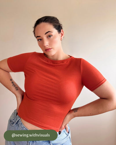 Person wearing a red crop top and blue jeans against a plain background
