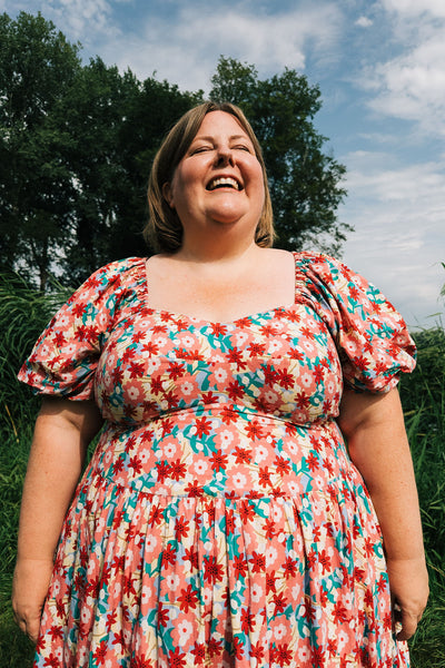 Woman wearing a floral dress standing outdoors with trees and blue sky in the background