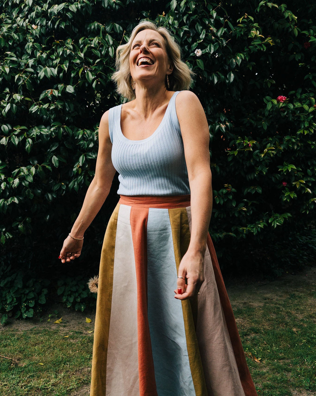 Woman laughing outdoors with a green bush and flowers in the background