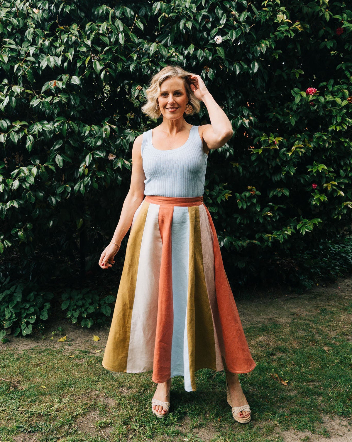 Woman standing outdoors with a green hedge background