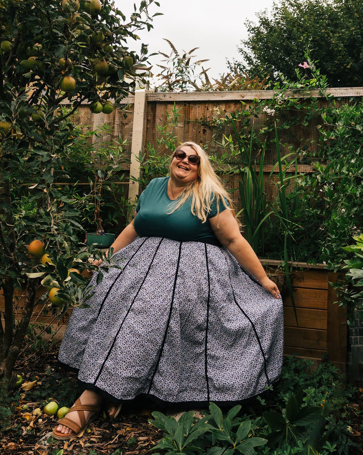 Woman in a garden wearing a green top and patterned skirt.