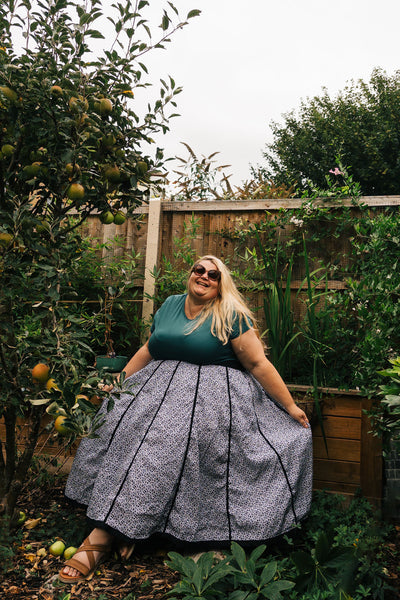Woman in a garden wearing a green top and patterned skirt.