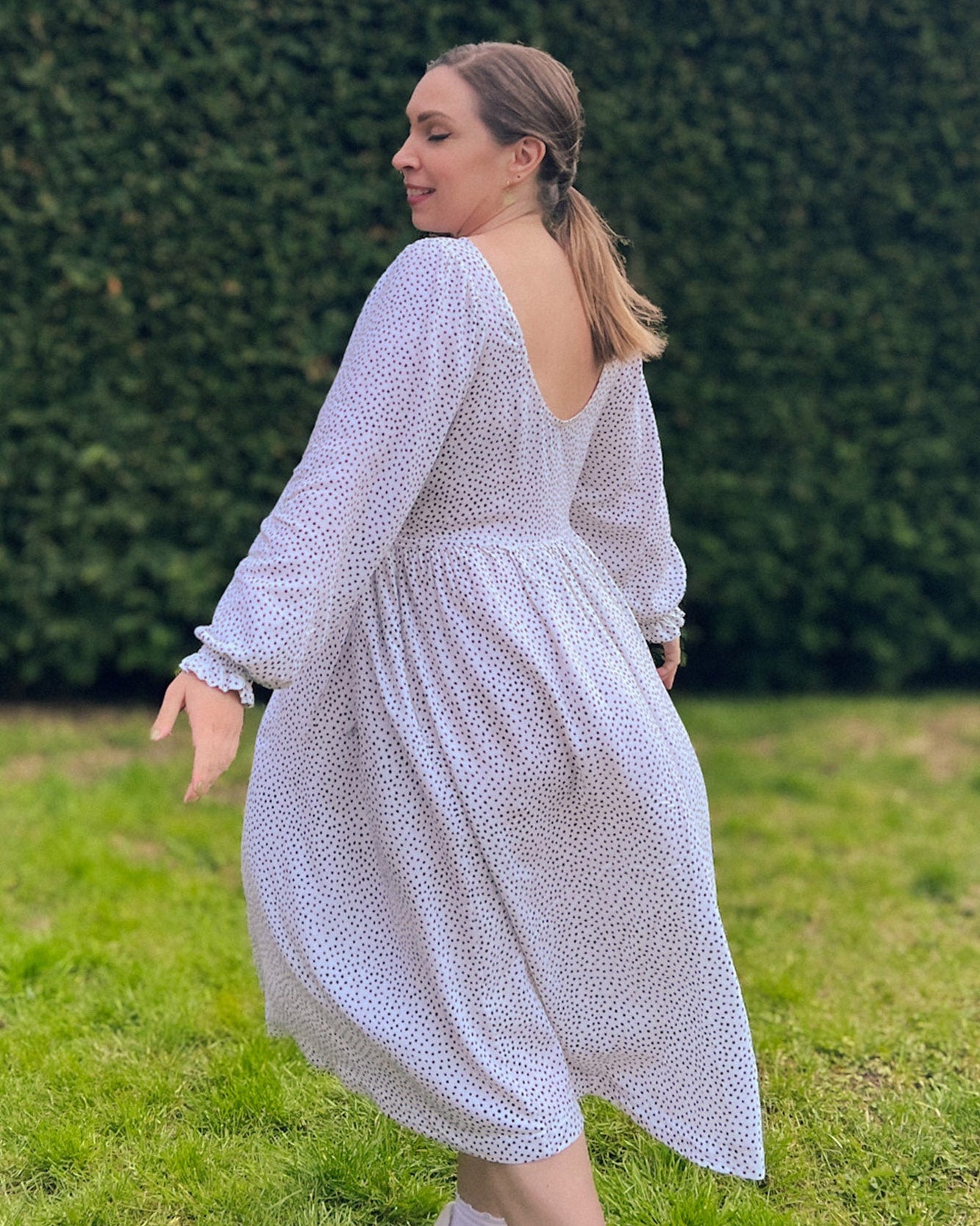 Woman in a light blue dress standing on grass with a blurred green hedge background